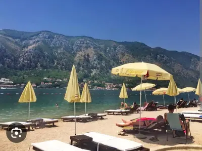 a beach with umbrellas and people sitting on the sand at Megy Apartment with parking and sea view in Kotor