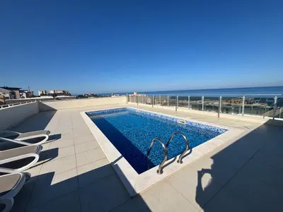 a swimming pool with chairs and the ocean in the background at Mira Apartment in Dobra Voda