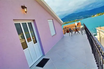 a pink house with a balcony with a table and chairs at Apartments Bella di Boka in Tivat