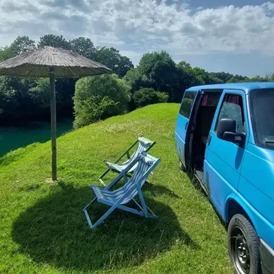 two lawn chairs and an umbrella next to a van at Camper t4 in Danilovgrad