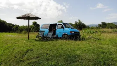 a blue van parked in a field with an umbrella at Camper t4 in Danilovgrad