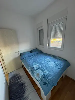 a bedroom with a bed with a blue comforter and a window at N&J apartman in Podgorica