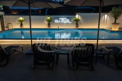 a table and chairs next to a swimming pool at night at Vila Kalina Apartments in Sutomore