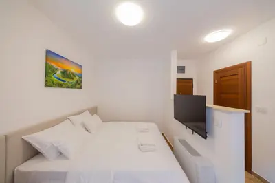 a bedroom with a white bed with a flat screen tv at Luča Apartments in Budva
