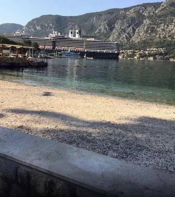 a beach with a cruise ship in the water at BMB Apartments Kotor in Kotor