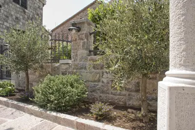 a stone wall with trees and bushes next to a building at Piazza Apartments 2 in Petrovac na Moru