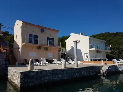 a house with chairs and a dock next to the water at Apartmani Bonaca in Tivat