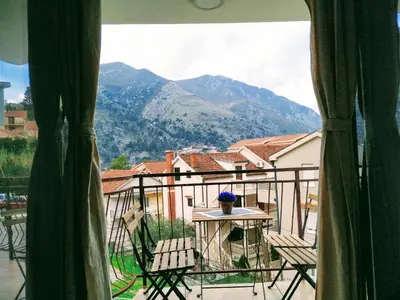 a balcony with a table and chairs and mountains at Rooms & Apartments Vukasović in Kotor