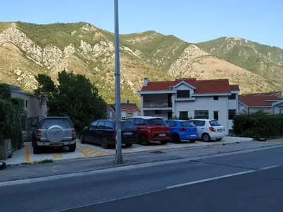 a parking lot with cars parked in front of a mountain at Rooms & Apartments Vukasović in Kotor