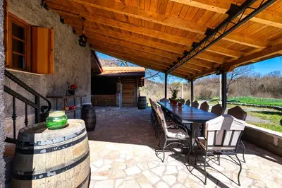 a patio with a table and chairs under a wooden roof at Handmade house Rijeka Crnojevica in Donje Selo