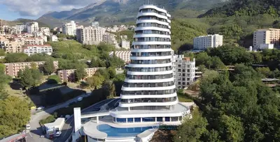 a large white building in front of a city at Luxe Beachfront Stay in Bečići with Pool in Budva