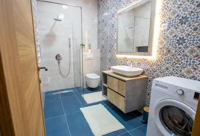 a bathroom with a shower and a sink and a washing machine at Bright & Cozy Apartment in quiet area near Airport in Golubovci