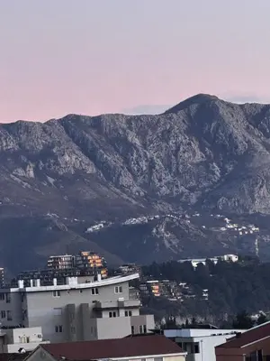 a large white building with mountains in the background at Апартаменти Будва in Budva