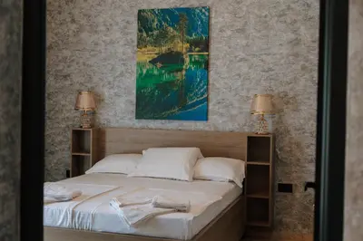 a bedroom with a bed with white sheets and two lamps at Hermosa Hotel in Donji Štoj