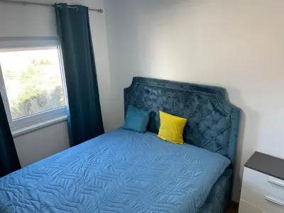 a bed with a blue headboard and two yellow pillows at Apartment with large living room in Bar