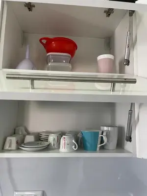 a white shelf with dishes and cups and a red bowl at Apartment with large living room in Bar