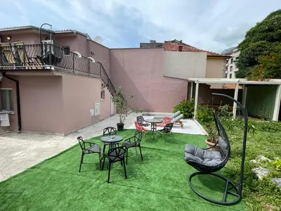 a patio with chairs and tables on a green lawn at Mystras Apartments in Kotor