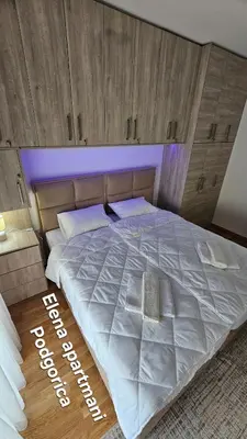 a bedroom with a large white bed with a wooden headboard at Elena apartmani Podgorica in Podgorica