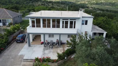 a white house with two people sitting at a table at Panorama Hill Apartments Ulcinj in Ulcinj