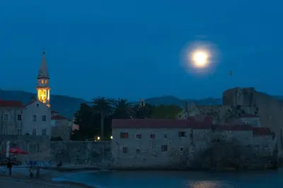 a moon rising over a city with a clock tower at Apartment Lucky in Budva