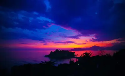 a sunset over the ocean with a rock in the water at Apartment Lucky in Budva