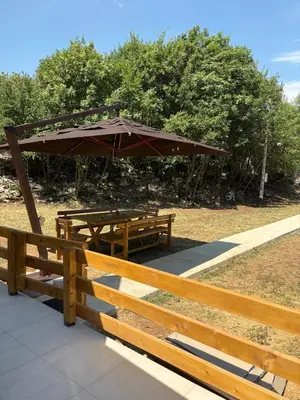 two picnic tables with an umbrella in a park at Wooden House Šapat sela in Podgorica