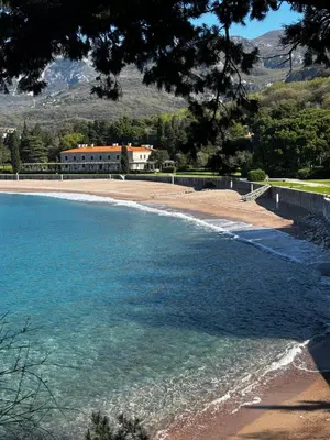a beach with blue water and a building in the background at Mind Wellness Montenegro in Sveti Stefan