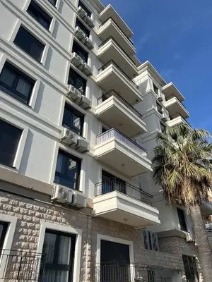 a tall white building with balconies and a palm tree at Alex apartment Bar in Bar