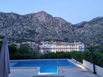 a cruise ship in a body of water with mountains at Studio apartment with heated pool in Kotor
