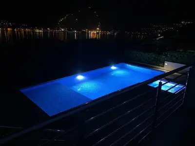 a swimming pool with lights on the deck at night at Sea view apartment with heated pool in Kotor