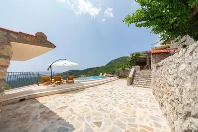 a patio with chairs and an umbrella next to a pool at Villa Jana Lapčići in Lapčići