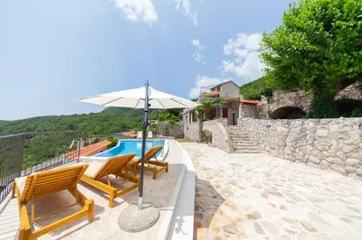 a patio with two chairs and an umbrella next to a pool at Villa Jana Lapčići in Lapčići