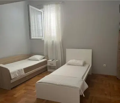 a bedroom with two beds and a window and wooden floors at sinbia apartment in Budva