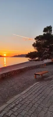 a bench sitting on the beach with the sunset at Apartmani Pavlović in Becici