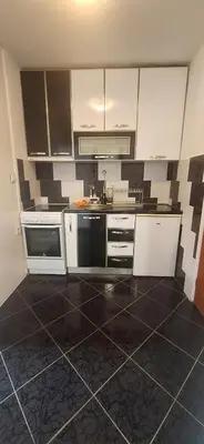 a kitchen with white cabinets and a black and brown tile floor at Apartman Budva in Budva