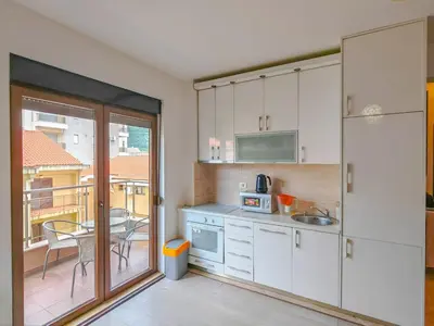 a kitchen with white cabinets and a table and a balcony at Seaside Nest Budva -Cozy Retreat 3 min from Beach in Budva
