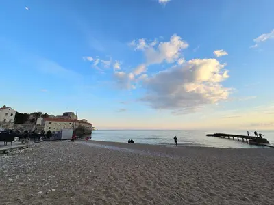 a beach with people and a pier and the ocean at Доброморе Будва in Budva