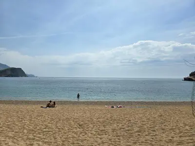 two people sitting on a beach with the ocean at Доброморе Будва in Budva