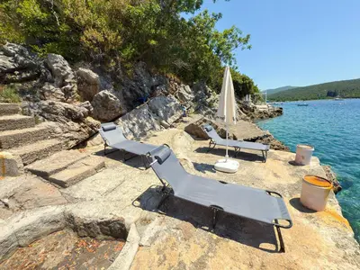 a group of chairs and an umbrella on a rocky shore at Apartmani Elena in Bigovo