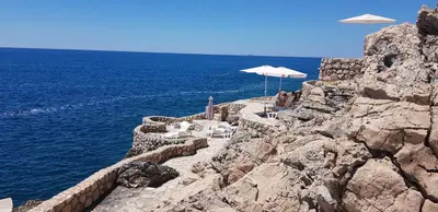 a cliff with chairs and umbrellas on the ocean at Emerald Dreamscape with Private Beach & Pool in Dobra Voda