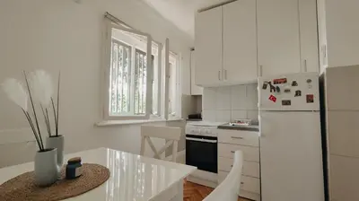 a white kitchen with a table and a refrigerator at Cozy & Bright Garden Flat in Podgorica
