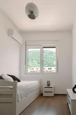 a white bedroom with a bed and two windows at Big Family apartment - 3BR in Budva