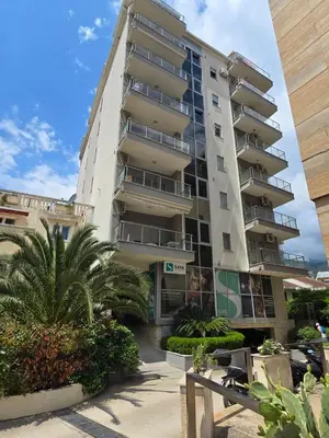 a tall apartment building with palm trees in front of it at Omega 3 Apartment Budva in Budva