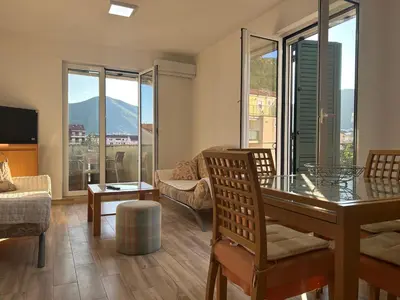 a living room with a table and chairs and windows at Green square apartment Budva in Budva