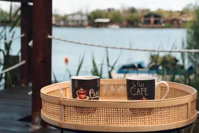 two coffee mugs sitting on a wicker table next to the water at River Breeze in Ulcinj