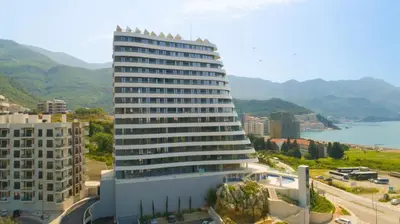 a tall white building with mountains in the background at Skyline Premium Residences Becici in Becici