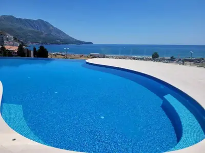 a large blue swimming pool next to a beach at Skyline Premium Residences Becici in Becici