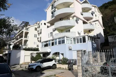 a white building with a car parked in front of it at Apartman Vuk in Budva
