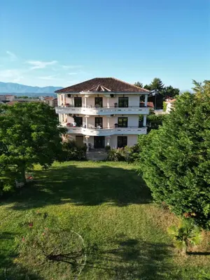 a large white building in a yard with trees at Antonios Apartments in Ulcinj