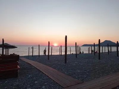 a sunset on a beach with poles in the sand at Ilino Studio Apartment in Bar